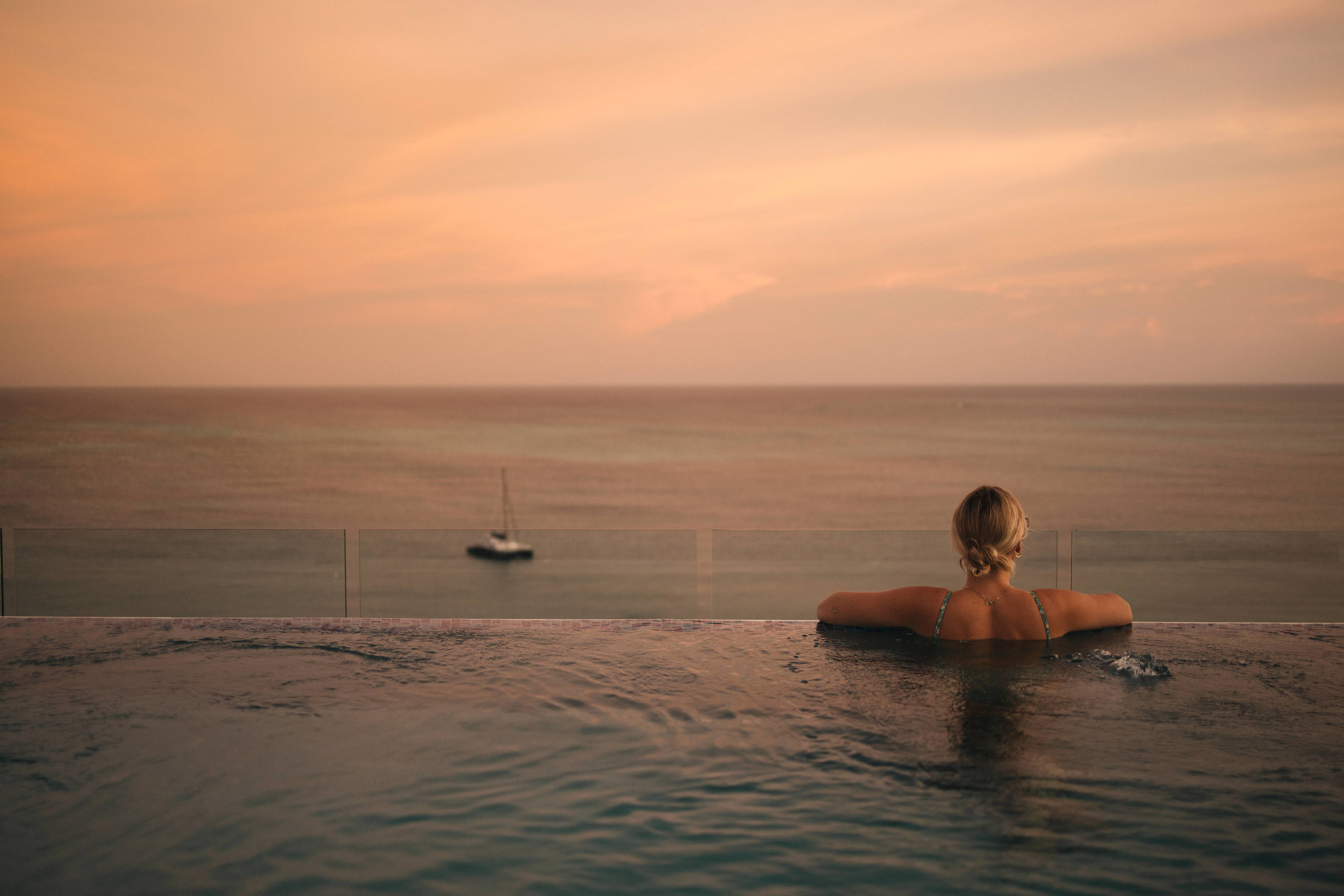 Mujer de espaldas en la piscina mirando el mar durante el atardecer