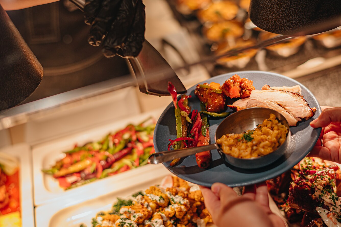 Hands holding a plate serving over a buffet with corn and turkey.