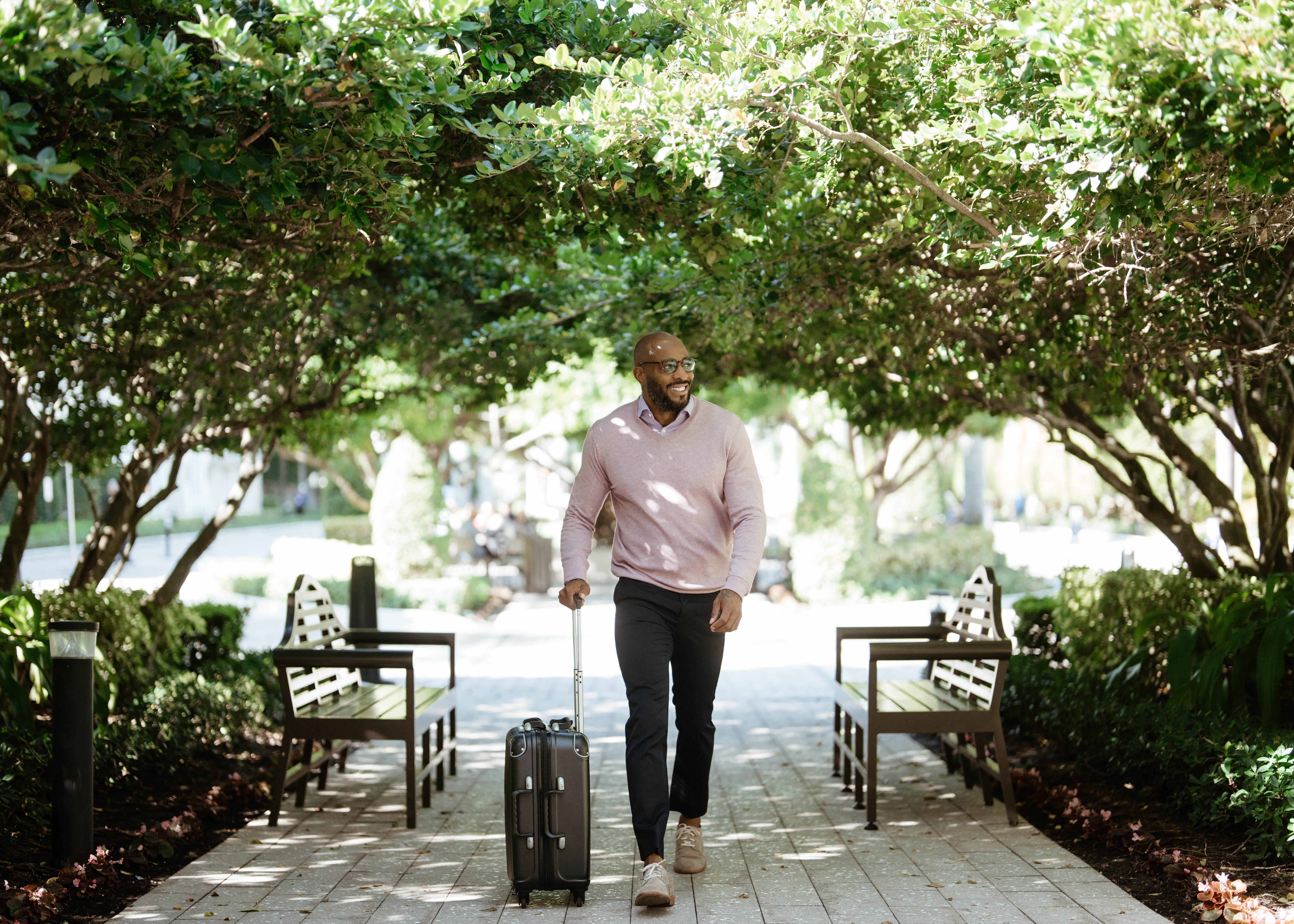 A man walking on a tree lined path with luggage 