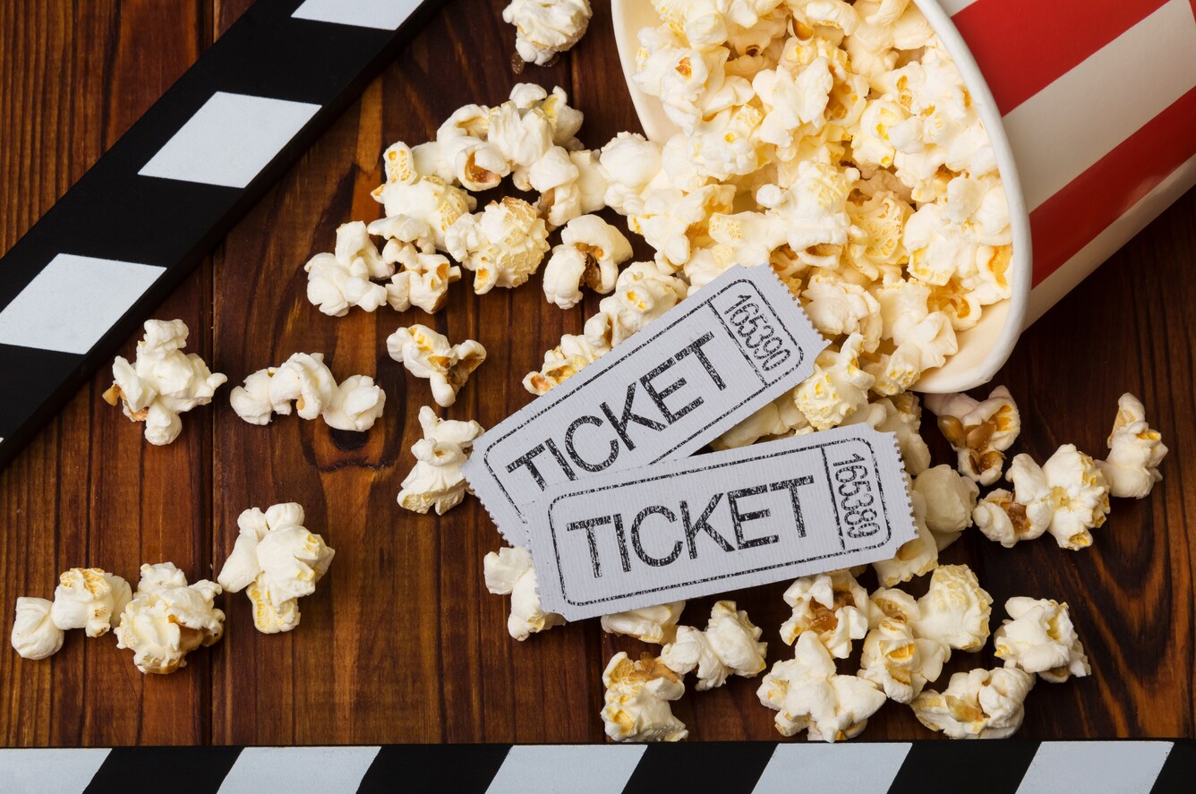 Movie tickets on top of popcorn spilling out of a bucket.