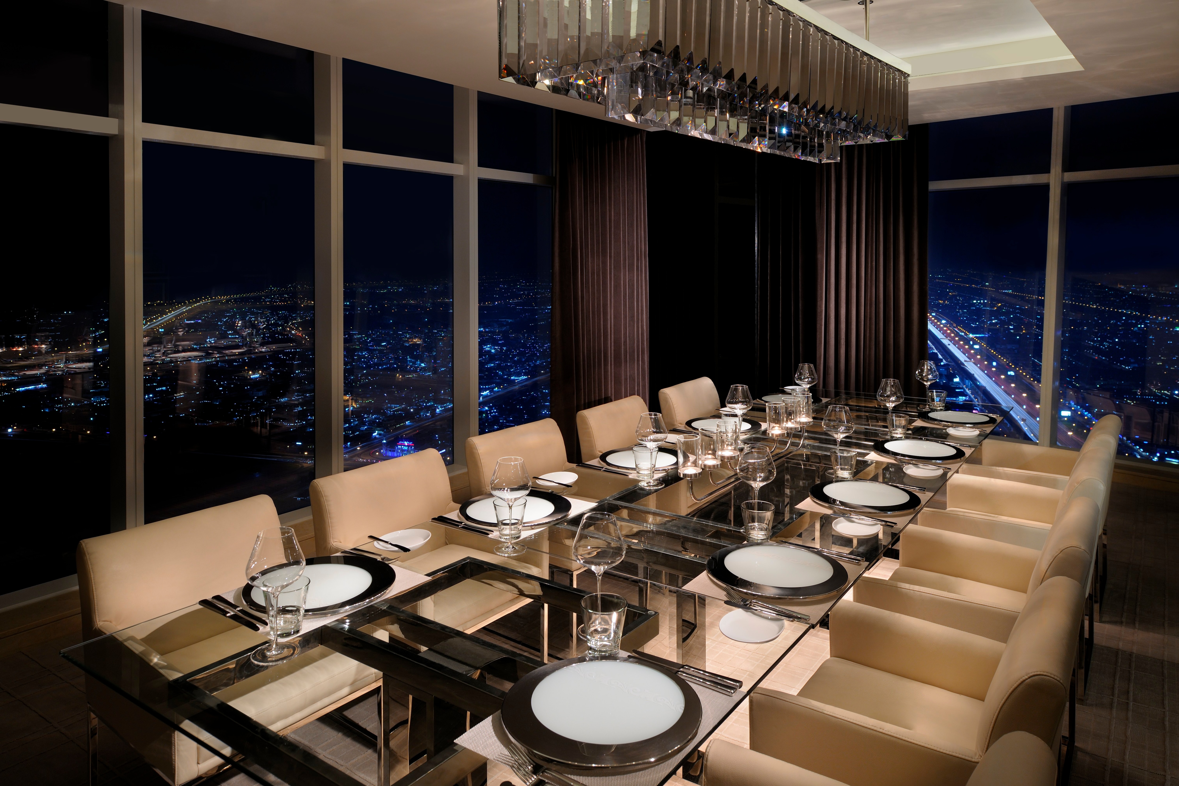 Restaurant dining table set beside windows with city views at night