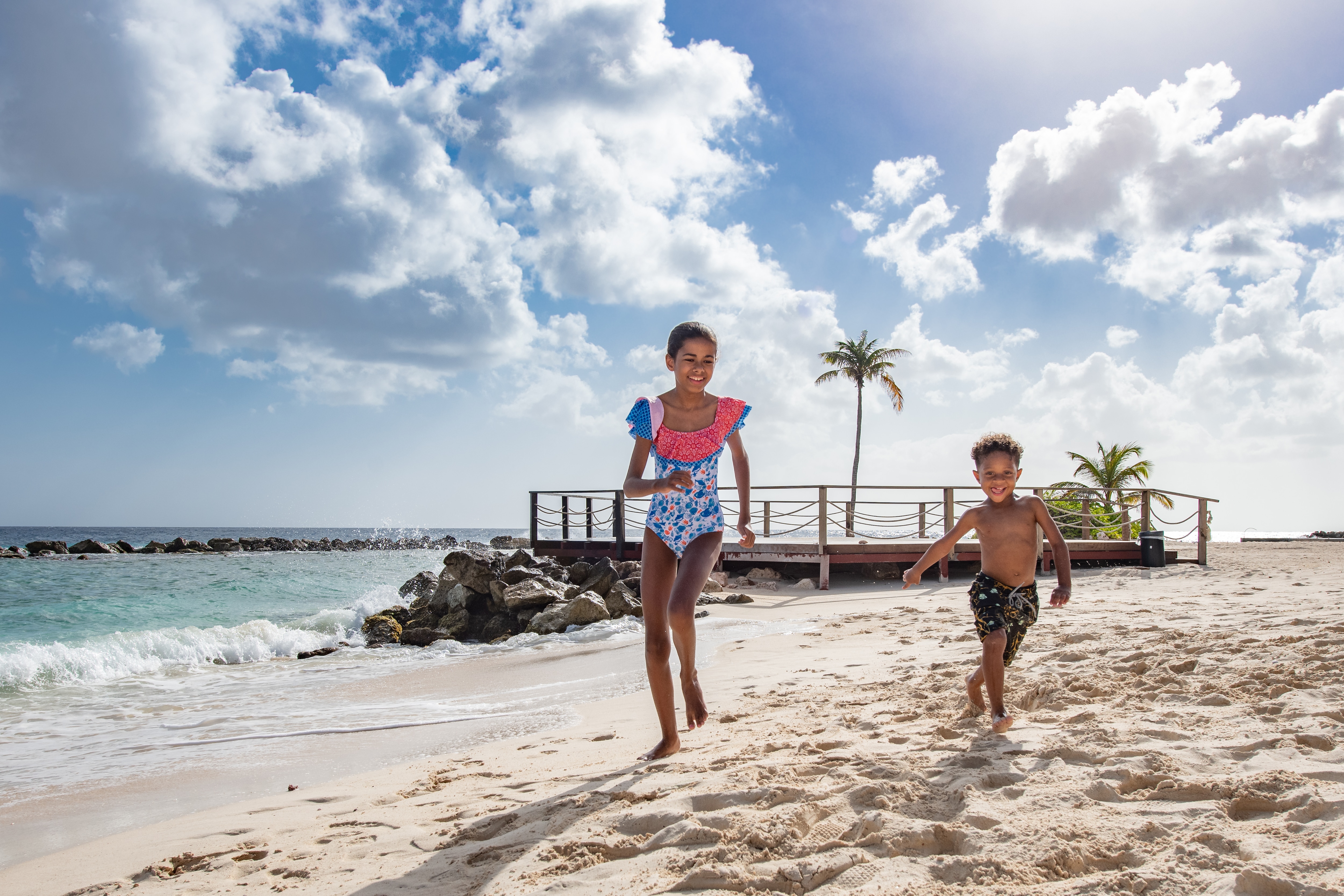 Crianças em trajes de banho correndo alegremente ao longo da praia