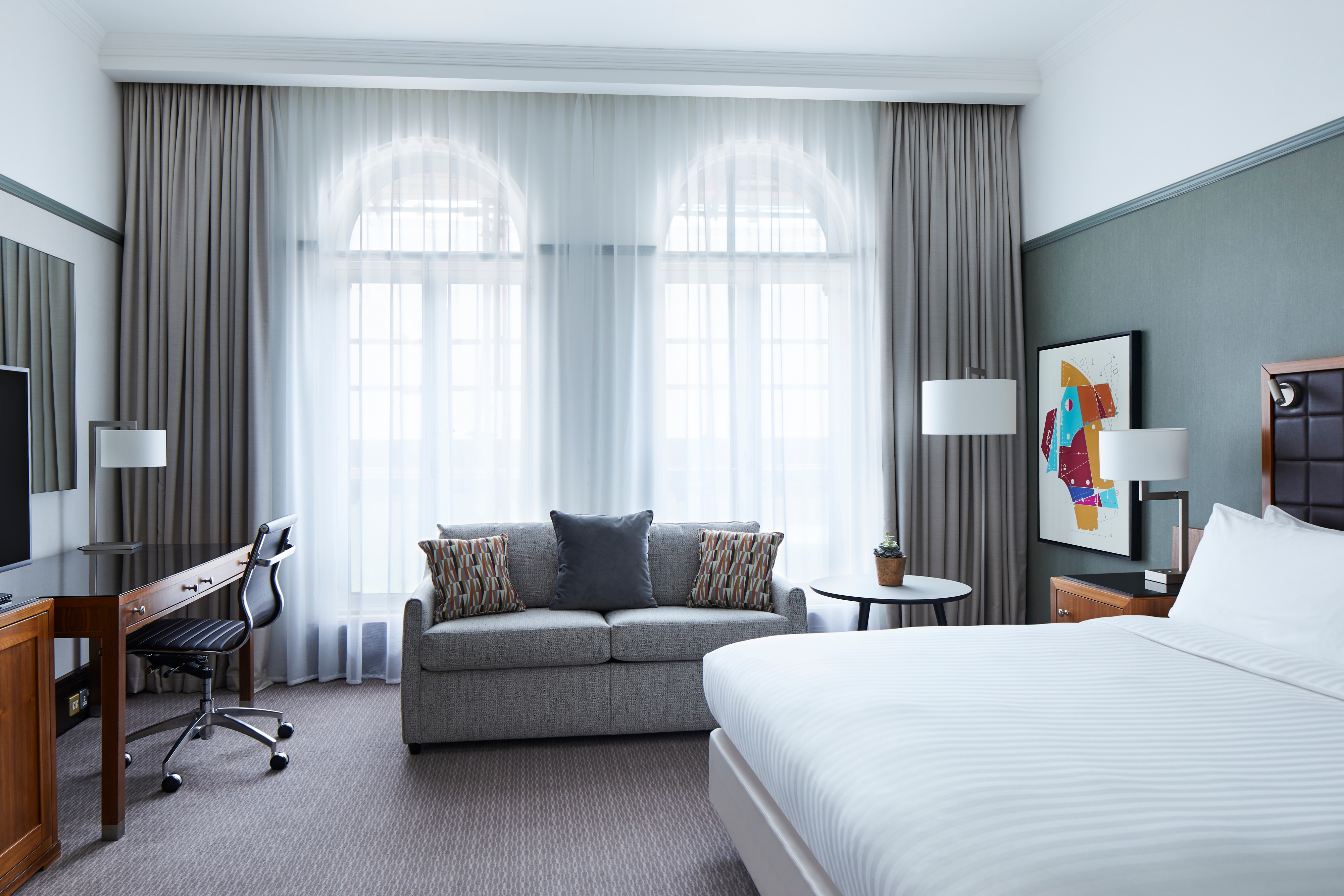 Room with bed, sofa, desk, art on walls and arched floor-to-ceiling windows