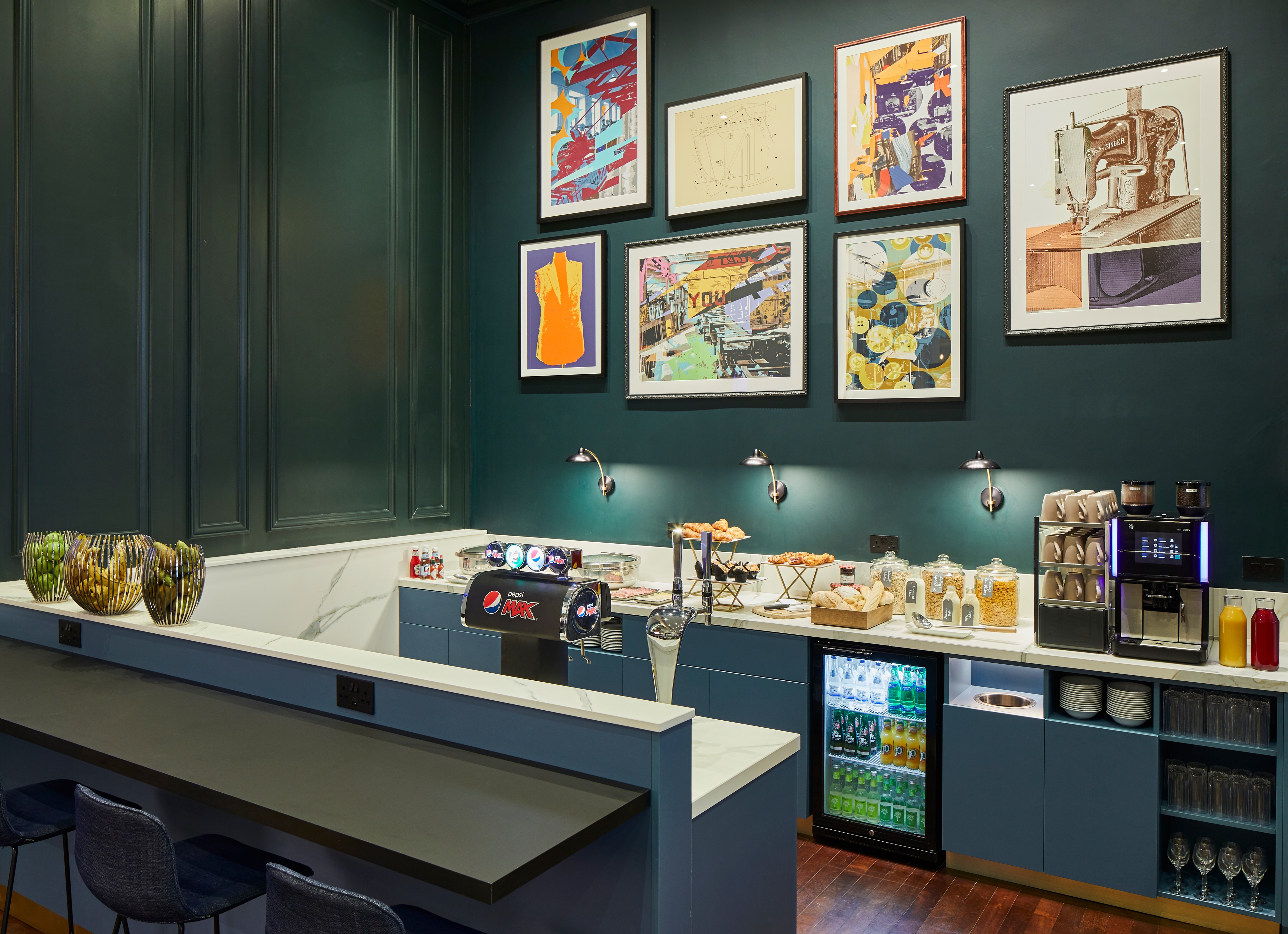 Counter displaying snacks and beverages in front of dark green wall with framed art pieces