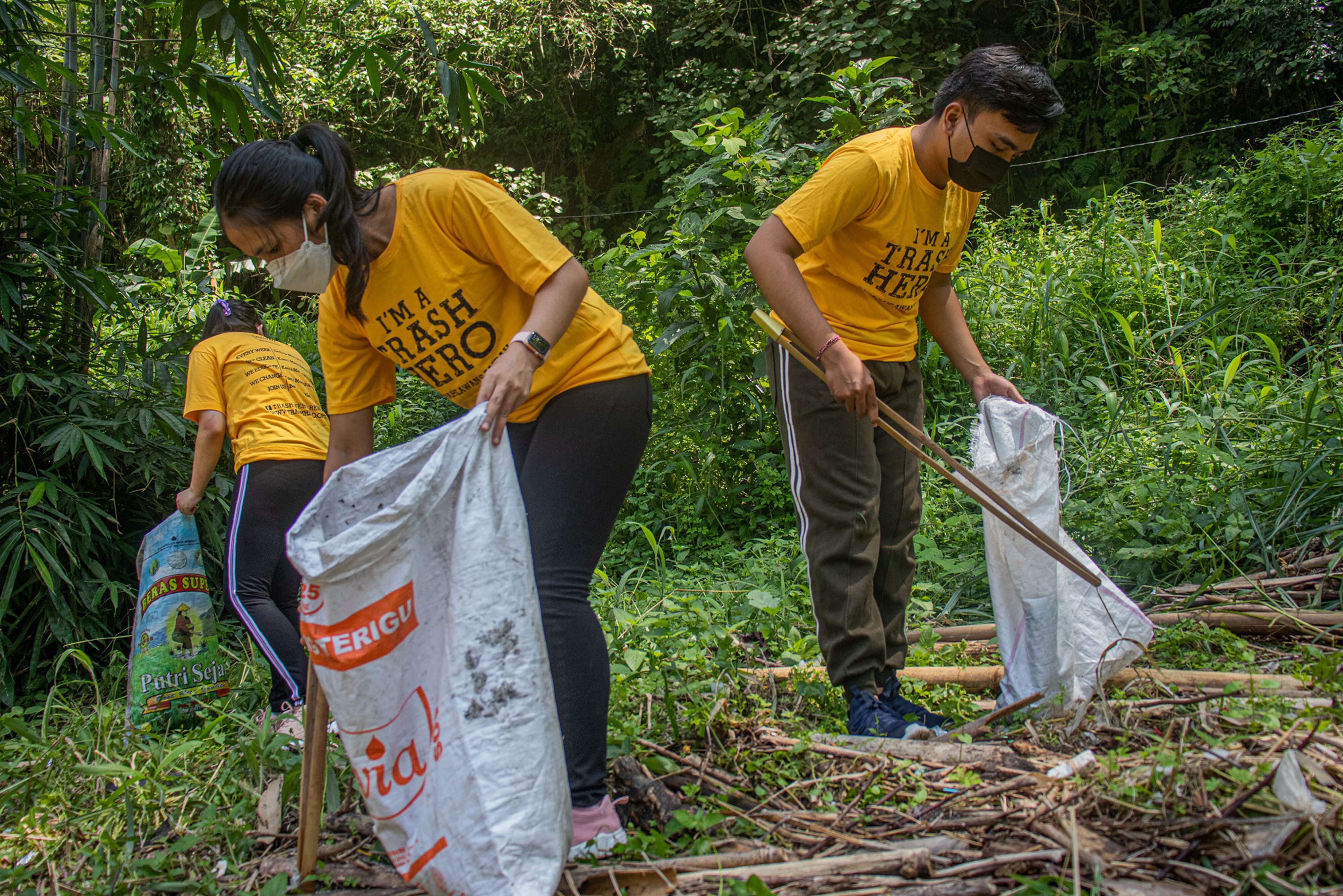 Trash Hero volunteers collecting trash near thick foliage 