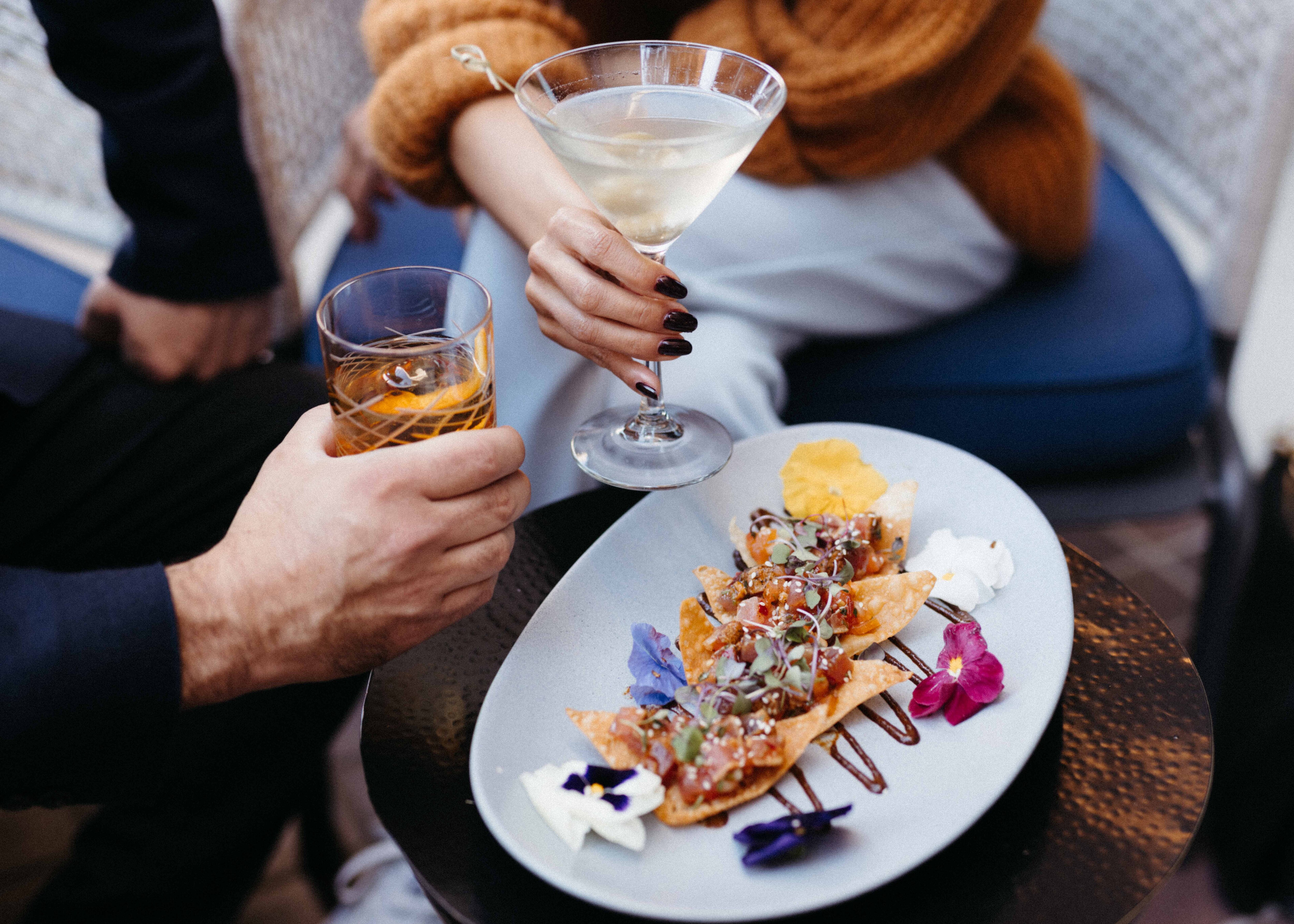 Hands holding cocktails, plus chips and salsa.