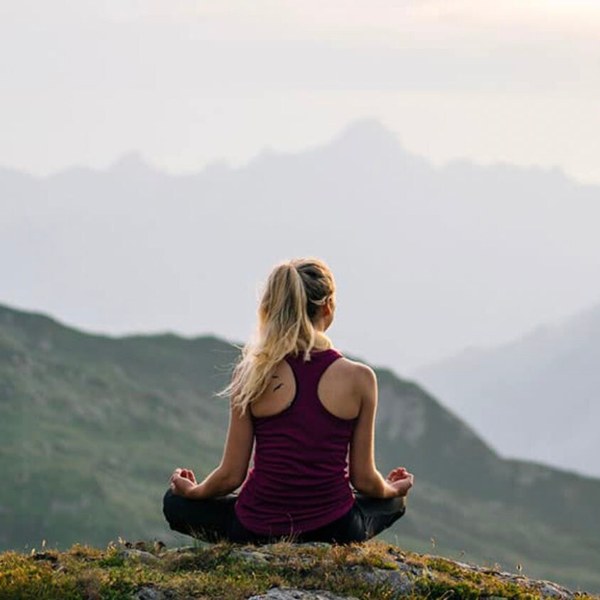woman meditating on a hill with mountains in the background