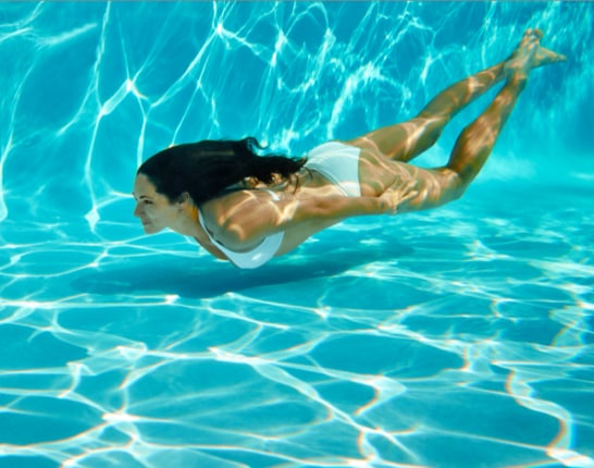 Woman in white bikini swimming underwater near the bottom of the pool