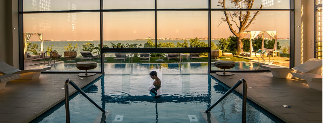 Spa style indoor/outdoor pool with towering window and a man standing in the water