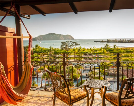 Balcony with table, chairs & a hammock overlooking the resort grounds and ocean beyond