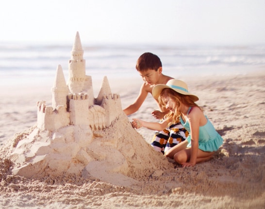 Two children on the beach building a large sand castle