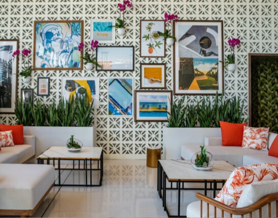 White modern sofas with orange throw pillows in front of a display wall of framed artwork