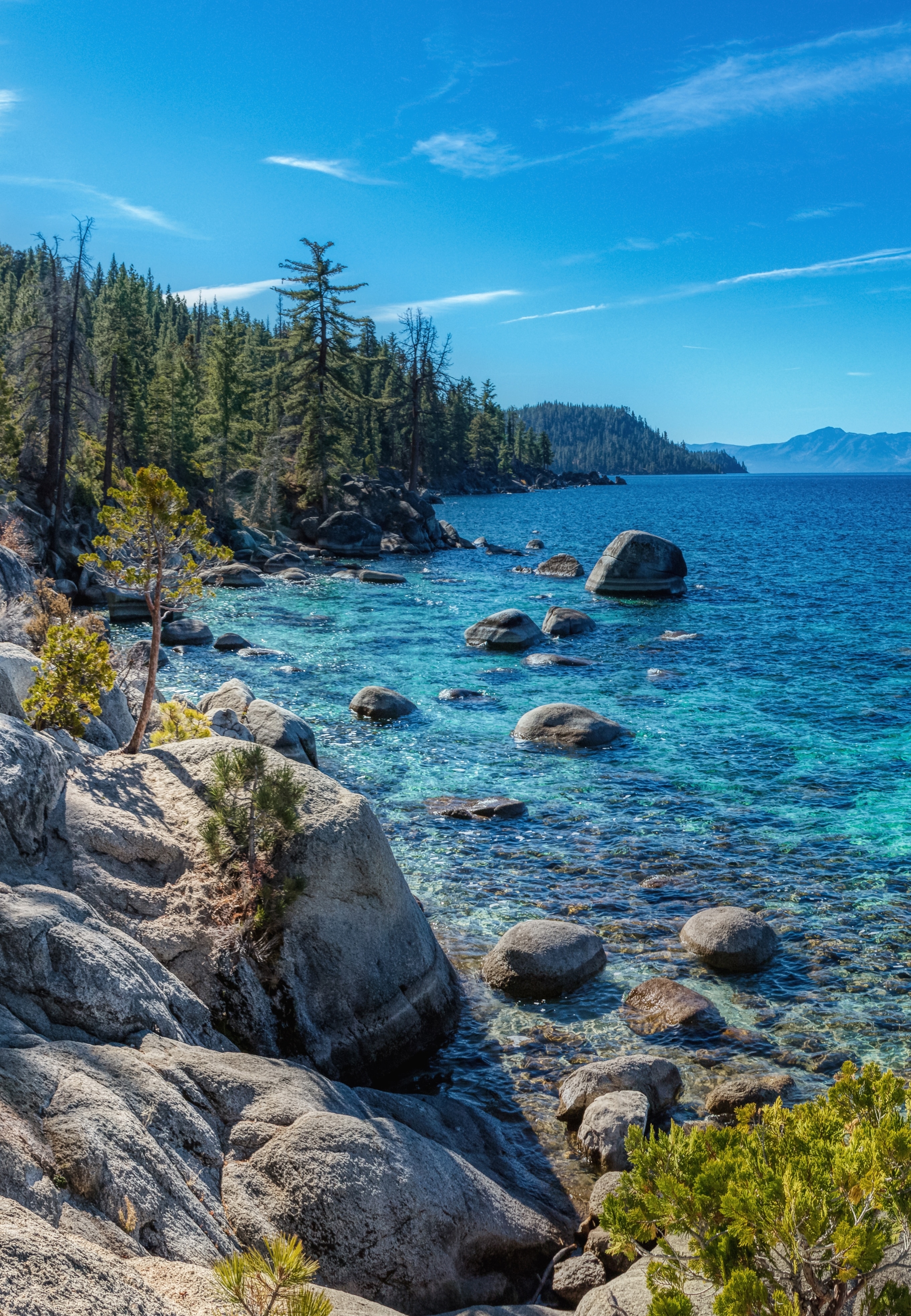 A dazzling blue lake is surrounded by rocky outcrops and towering pine trees at Chimney Beach in Lake Tahoe, California