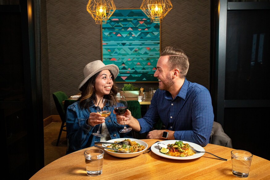 A romantic couple wearing blue shirts enjoy dinner in dimly lit room.