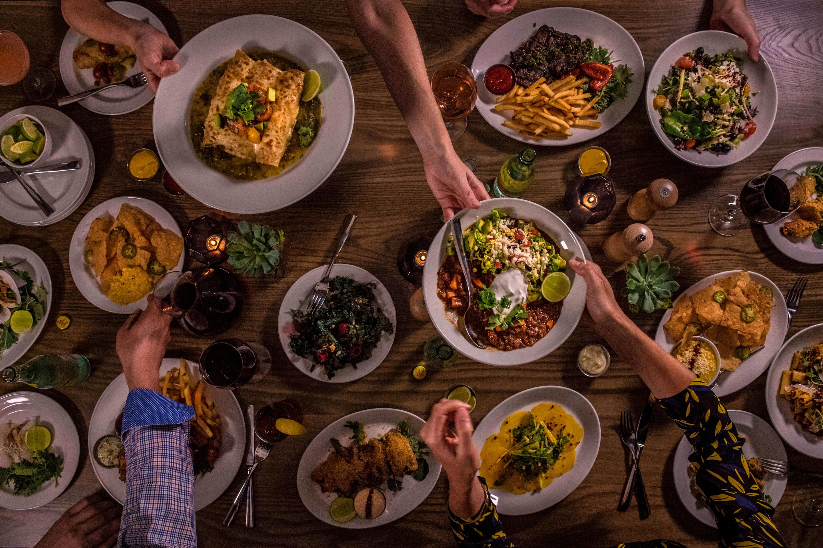 overhead view of lots of plates with food on them, and hands reaching in.