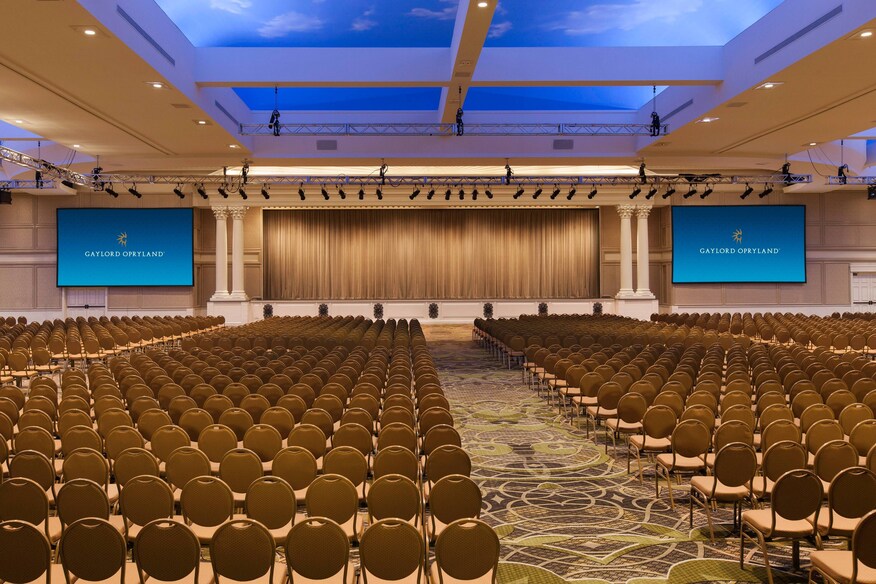 Large ballroom with hundreds of seats facing a lecturn and two large screens.