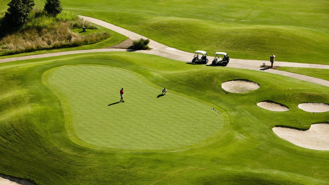 Golfing green with golfer, and cart near sand trap.
