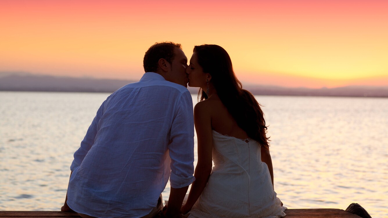Man and woman kissing during the sun setting over the water