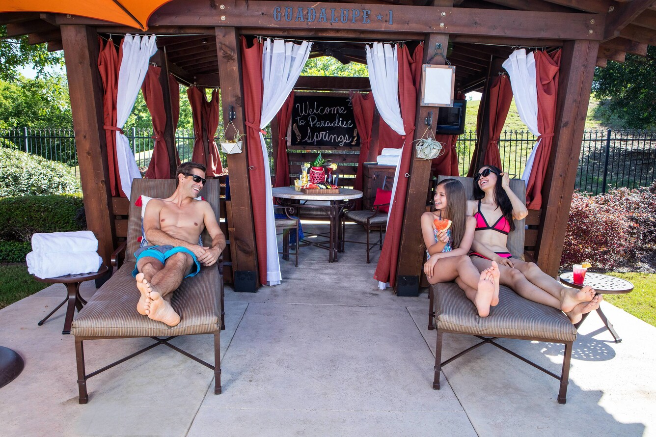 Family lounging on chairs in the shade by their cabana with dining table and curtains