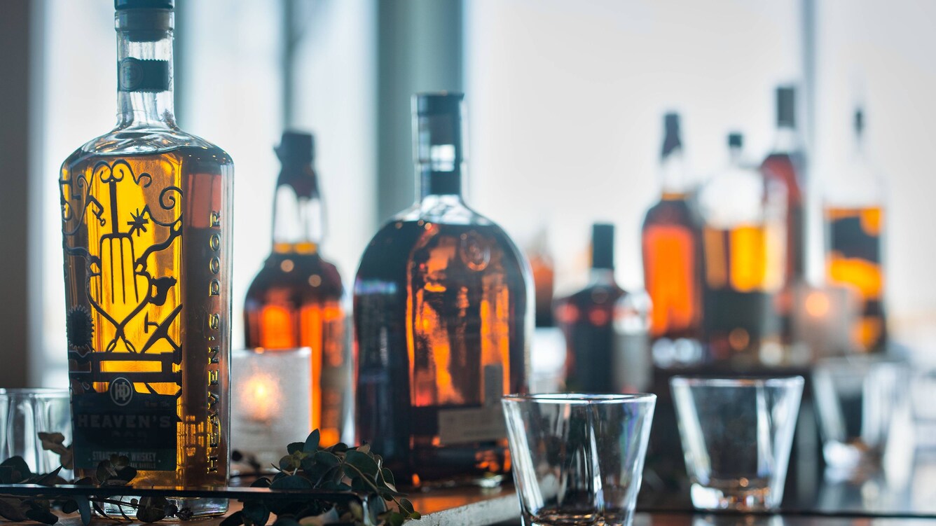 Various types of golden liquor aligned on the counter with whiskey glasses