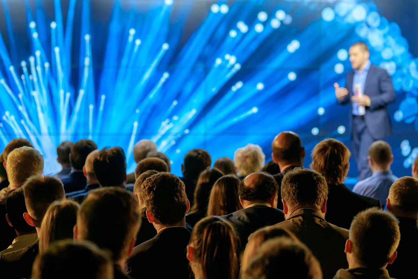 Man performing on stage with blue lights shooting in background with crowd below