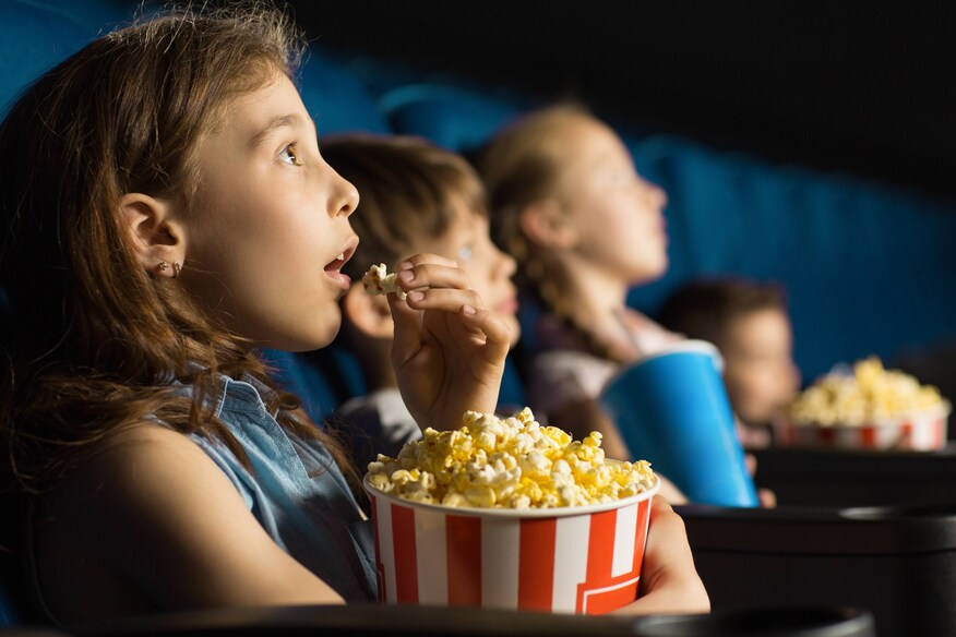 Children watching a movie and eating popcorn.