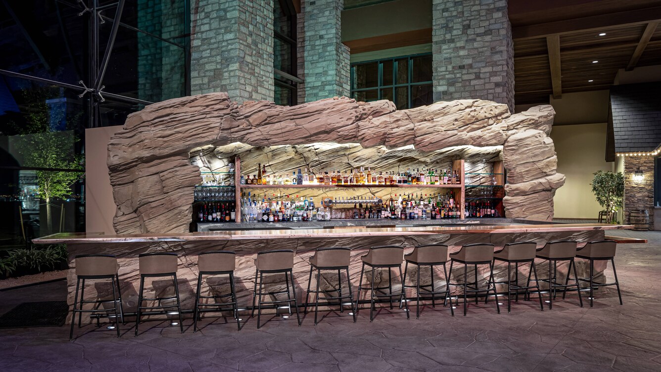 Empty barstools at the bar with a view of the shelved bottles of spirits.
