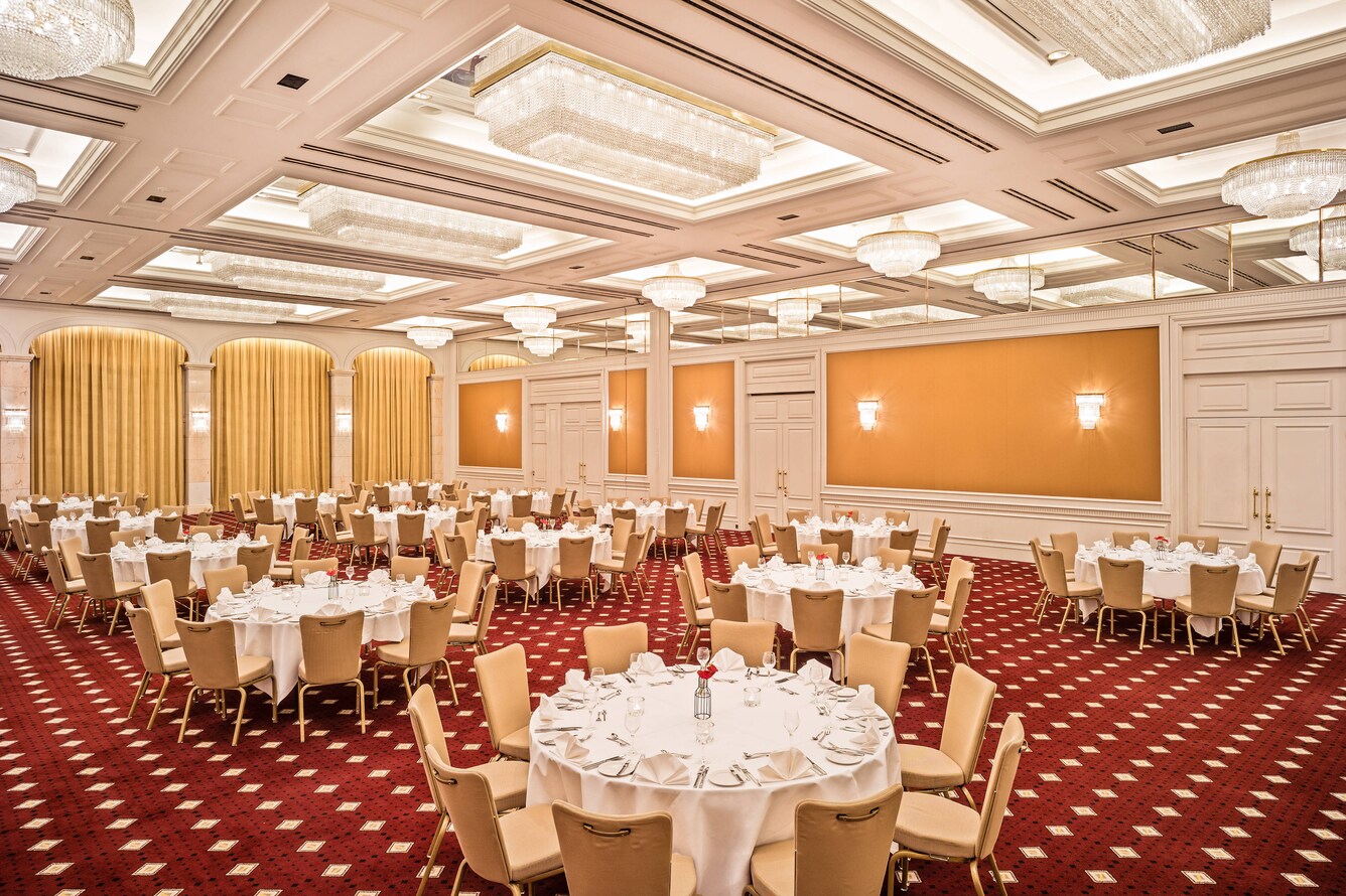 Large ballroom with round tables in white linen on red carpet