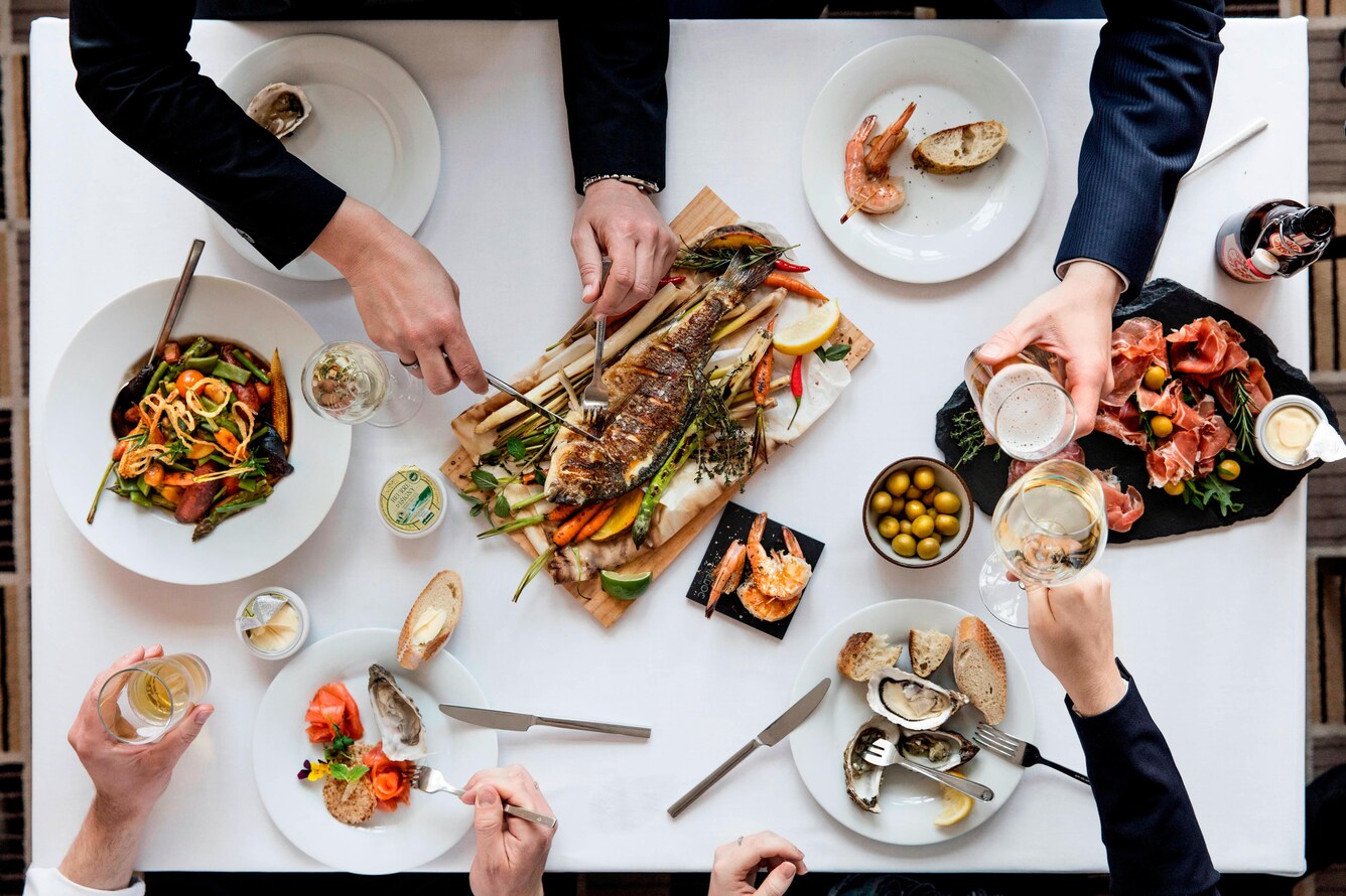 Overhead view of a variety of foods with many hands reaching in
