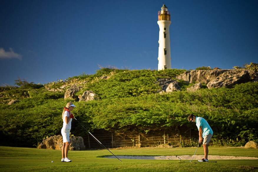 Man and woman playing golf with a lighthouse in the background.