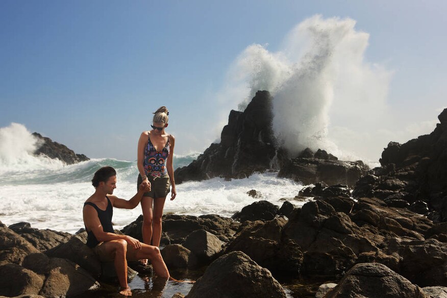 Man and woman on a rocky shoreline with waves crashing in the background