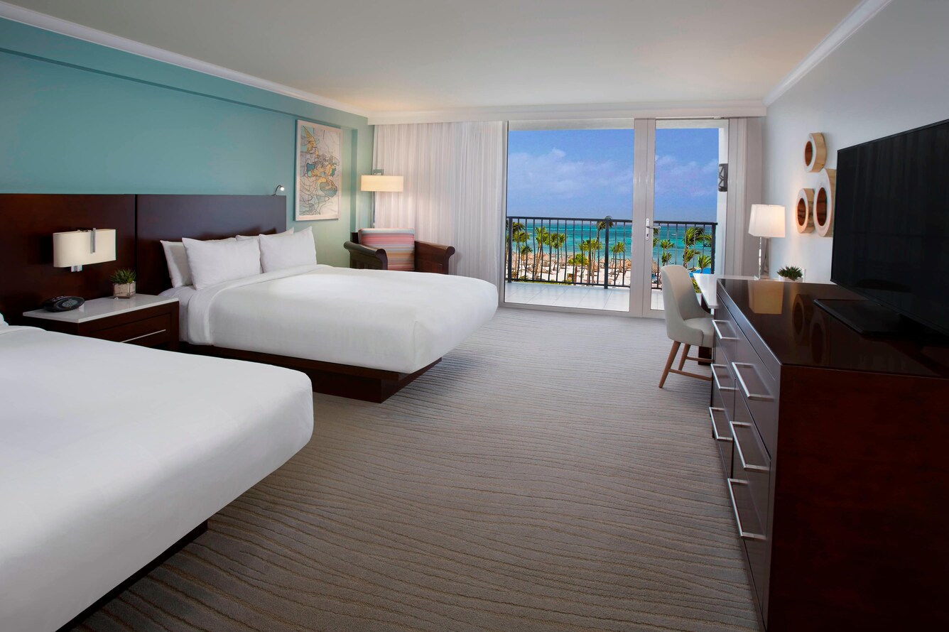 Guestroom with two queen beds and a premium view of the balcony, ocean, beach, and trees.