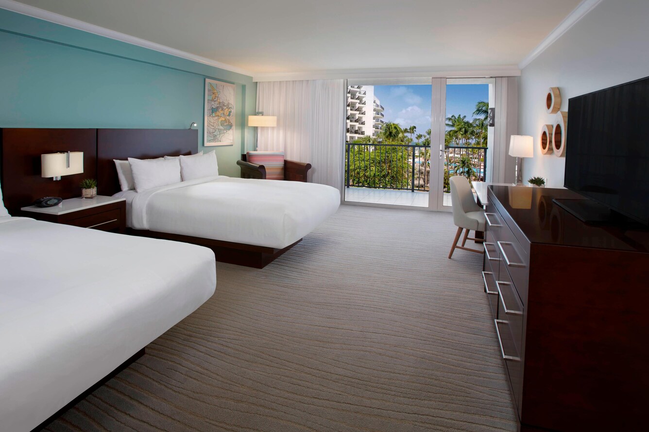 Guestroom with two queen beds and a view of the balcony and garden area.