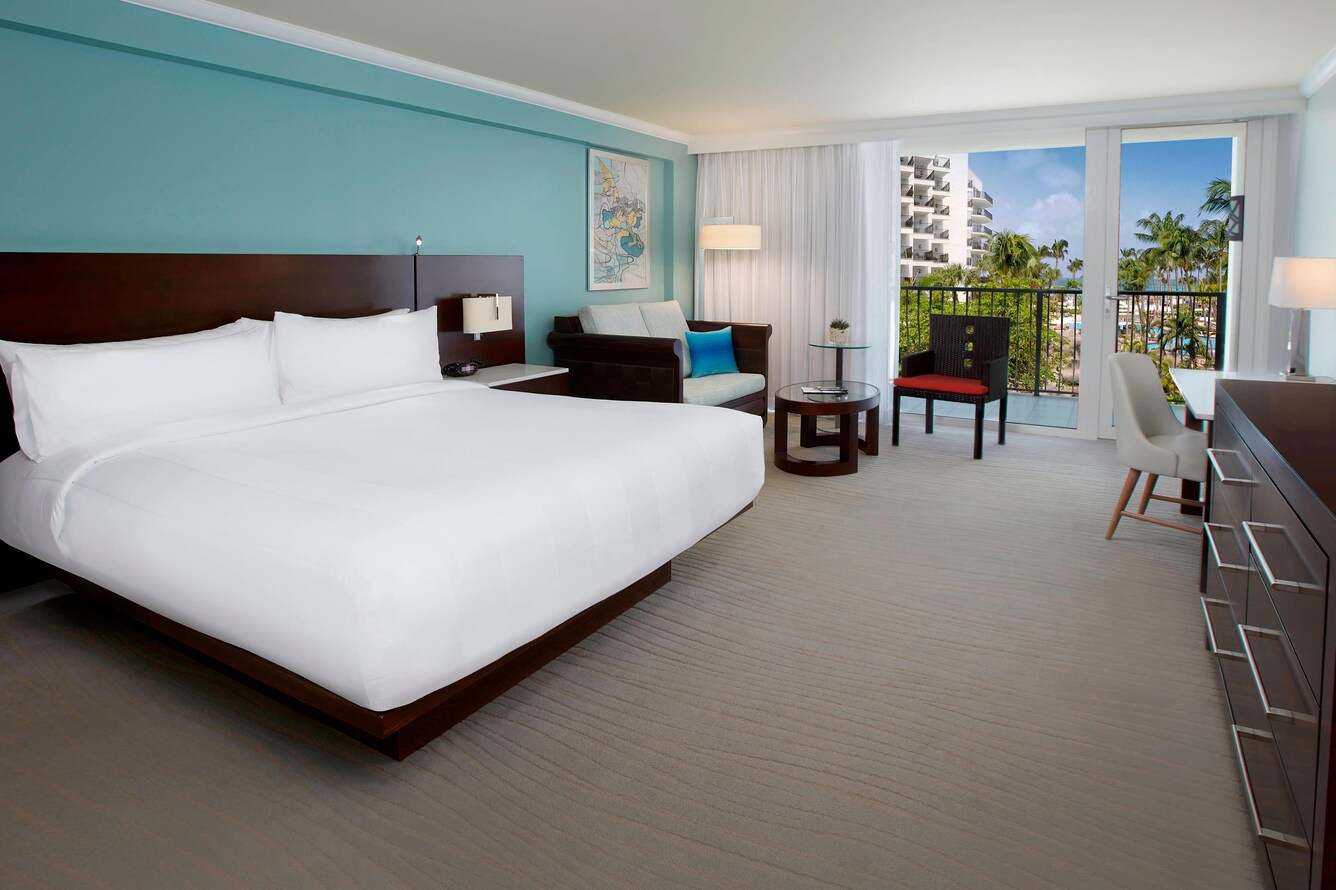 Guestroom with a single king bed, table with chair and view of the balcony and garden.