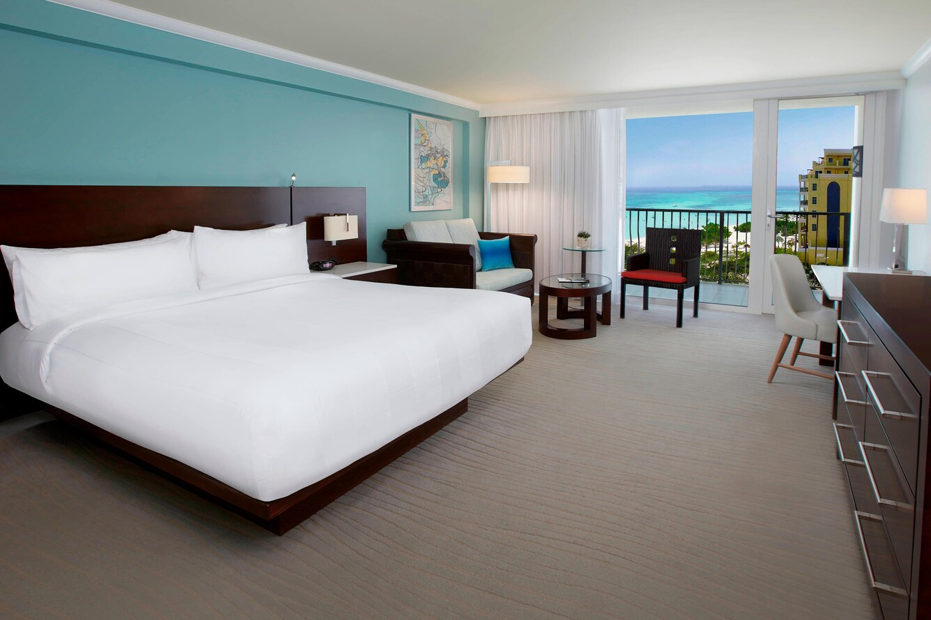 Guestroom with a single king bed and a partial view of the balcony, beach, ocean, and trees.