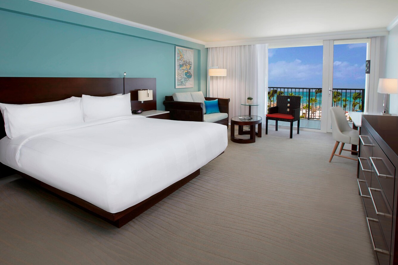 Guestroom assorted furniture, single king bed and view of the balcony, beach, ocean, and trees.