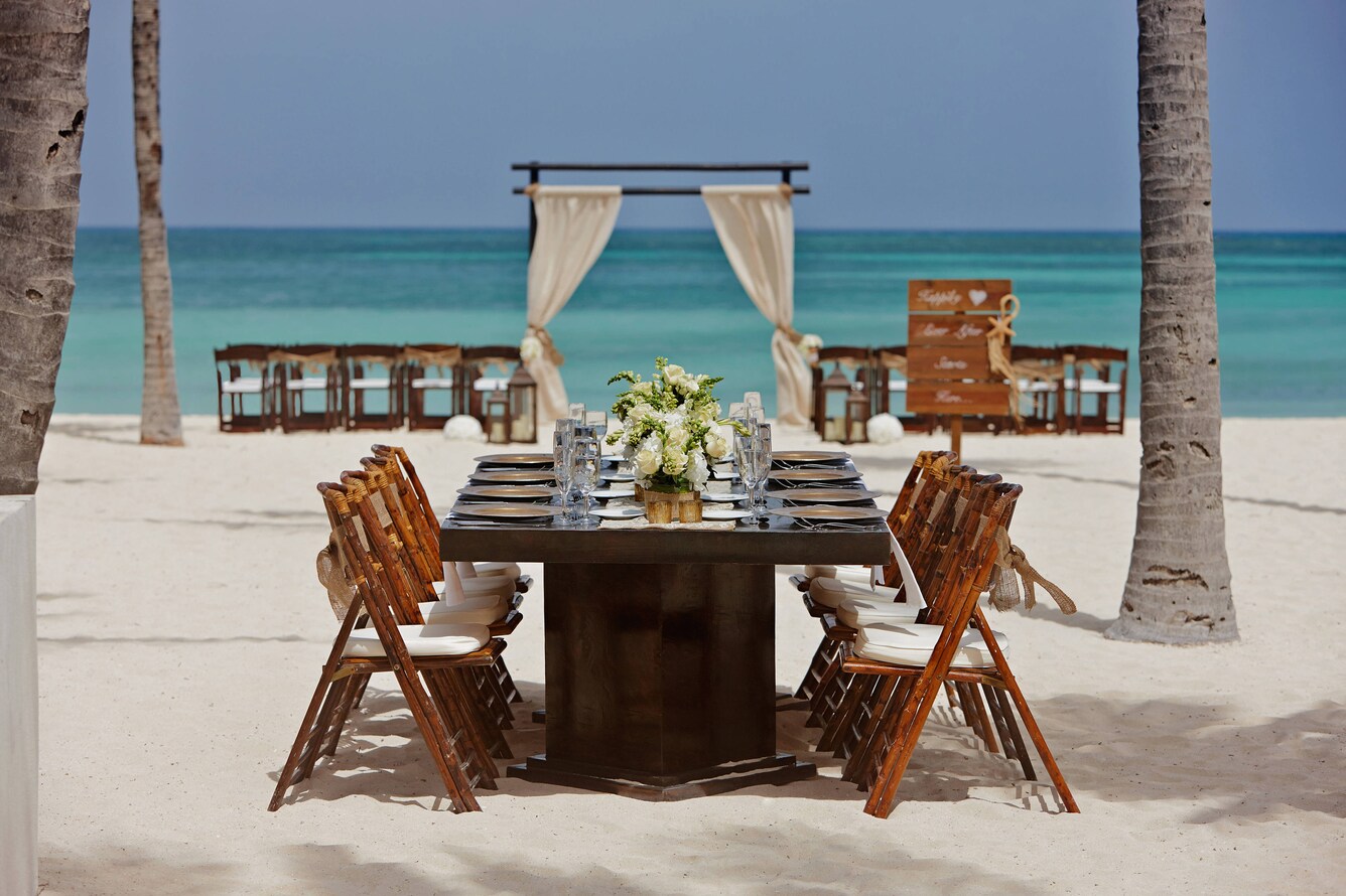 Beach sitting arrangements and and a long dinner table with chairs prepared for a wedding.