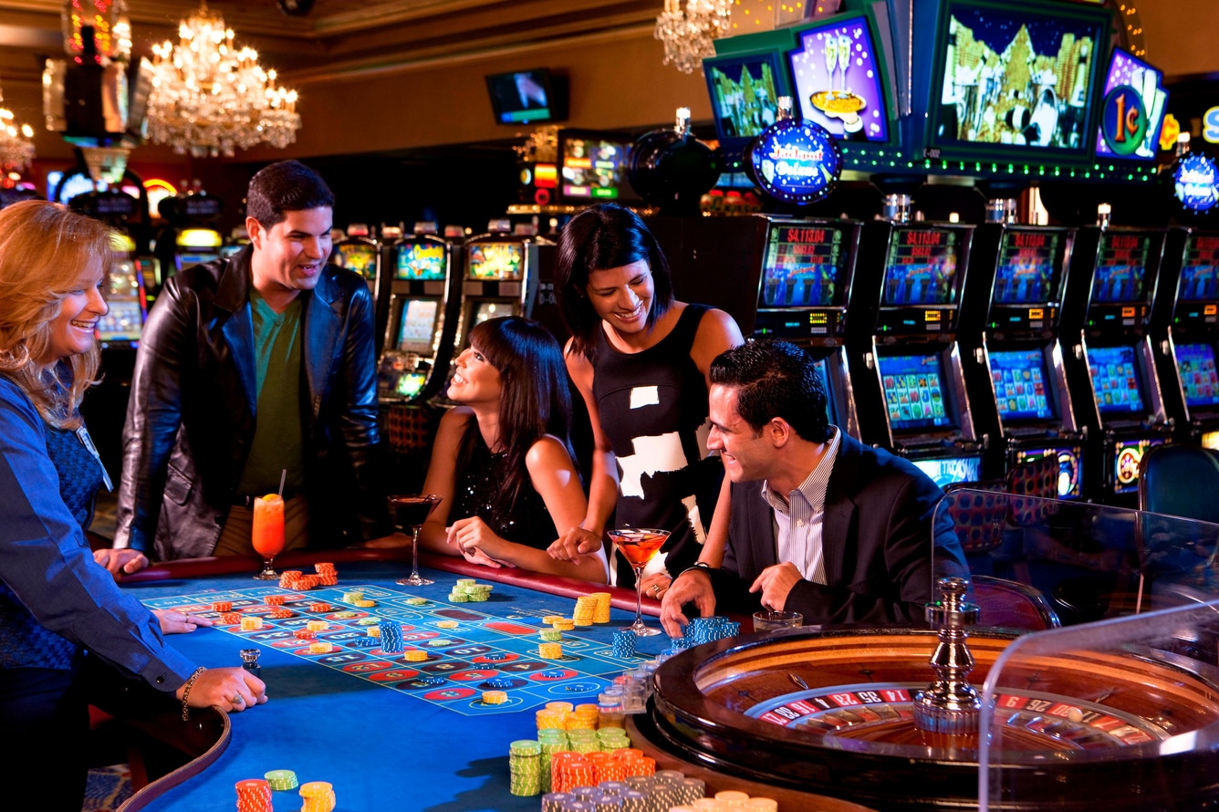 Group of adults at casino table with slot machines in background