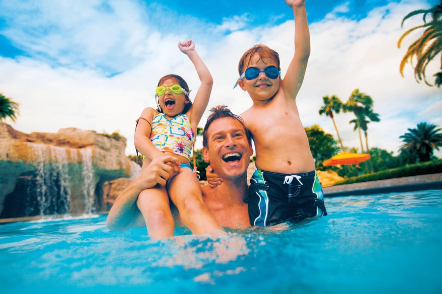 Family playing in the outdoor pool with waterfall in background