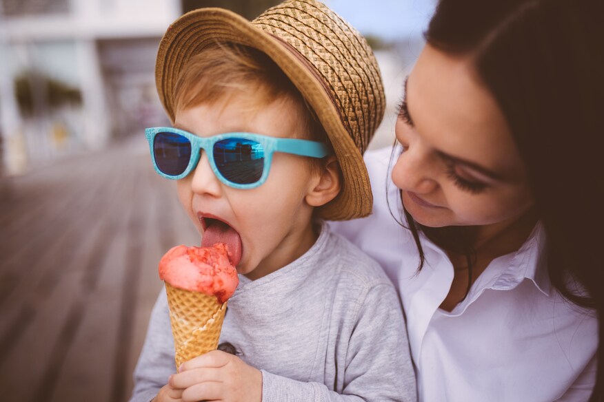 Young boy being held by his mother and licking an ice cream cone.