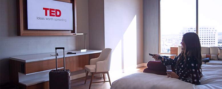 Woman laying in bed watching TED talks on the television