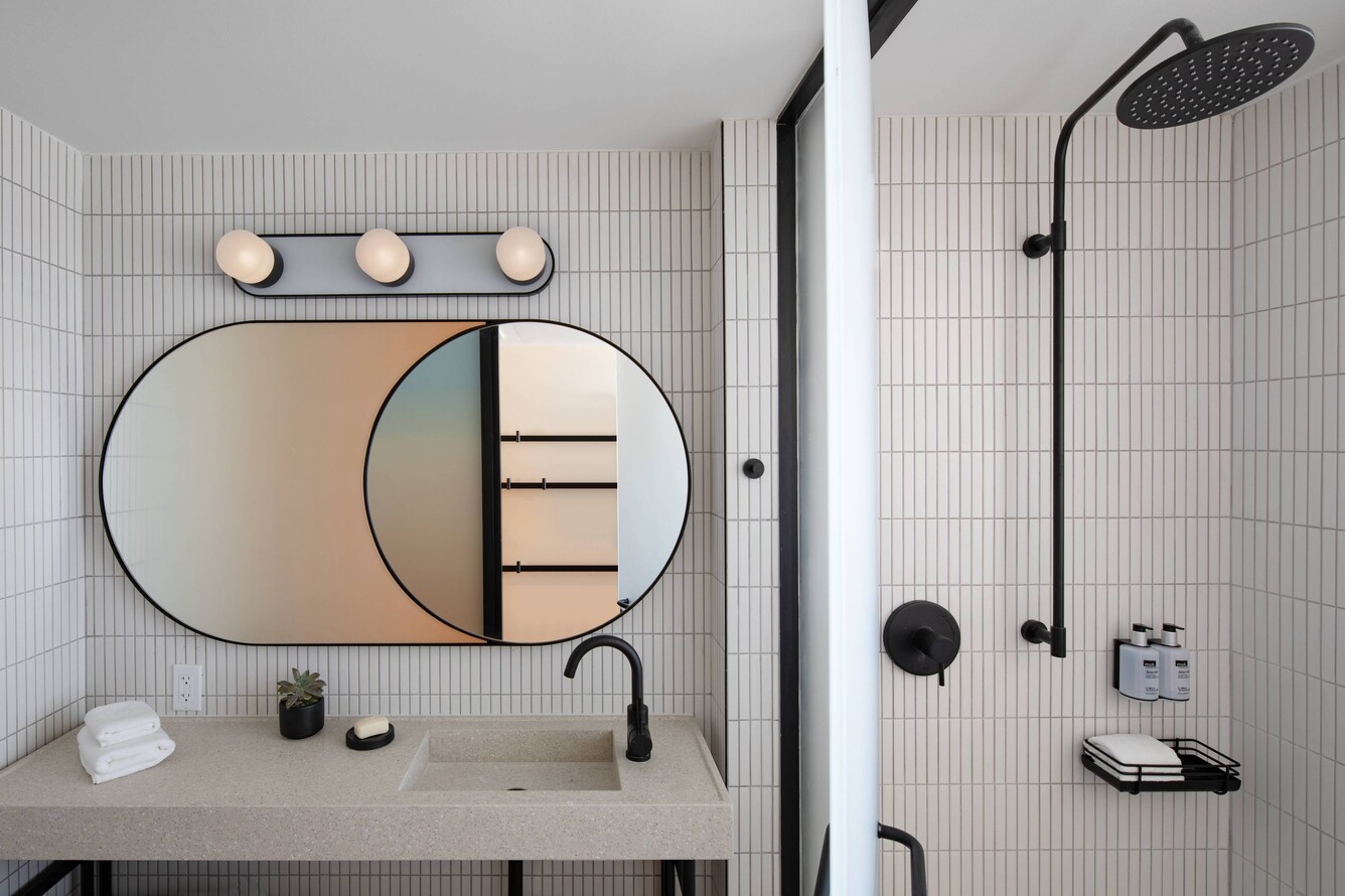 Guest bathroom with white tile, oval mirror, and black fixtures