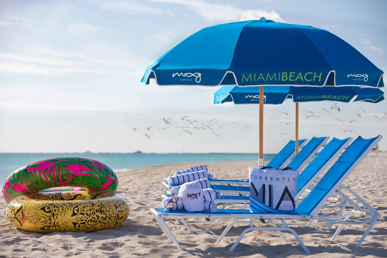 Miami beach sand and water with Moxy's blue umbrella and multi-colored floaties
