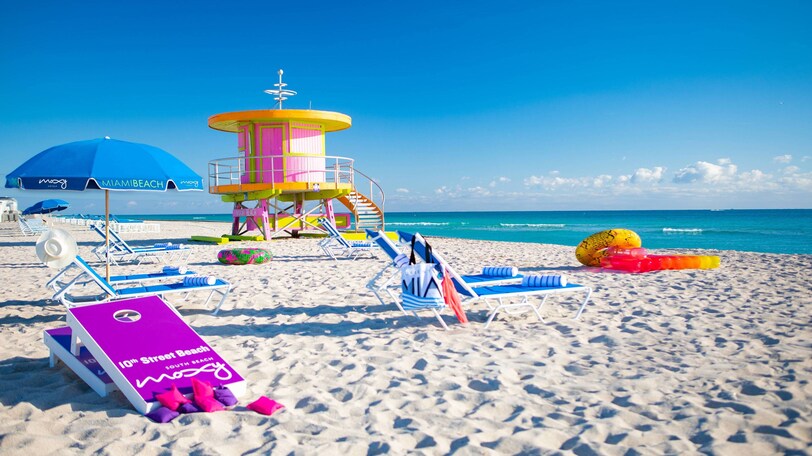 Lounge chairs, sun umbrellas, beach game pieces and inflatables sitting on a sandy beach.