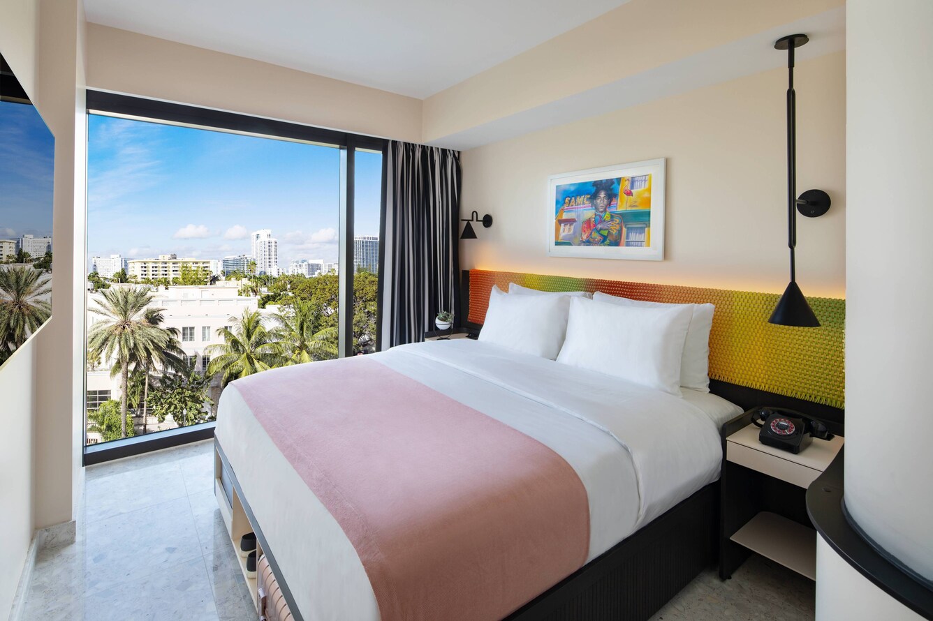 King bed with pink coverlette and large floor to ceiling windows with palm trees
