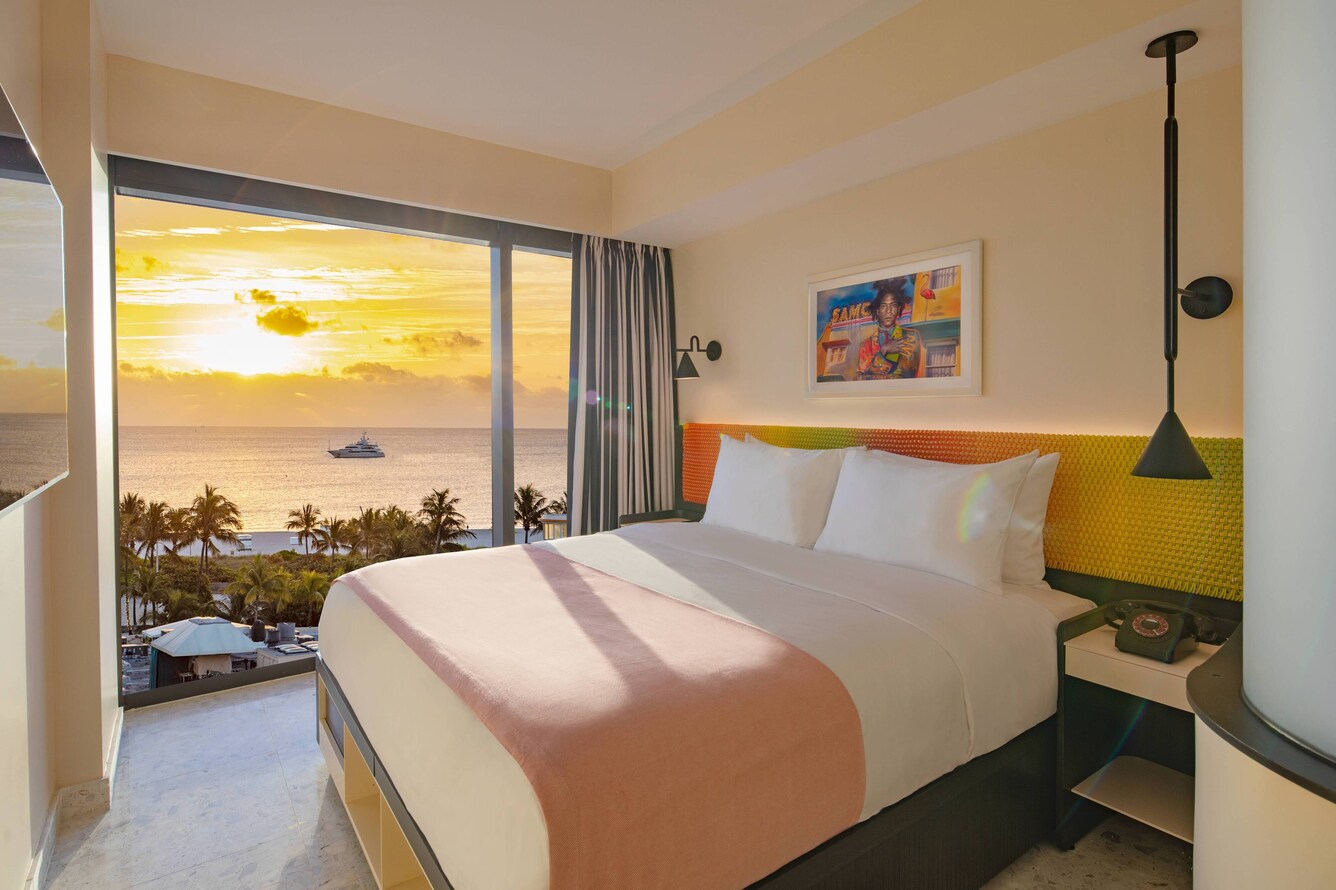 King bed with pink bedding decor, large windows with view of sunset over the water
