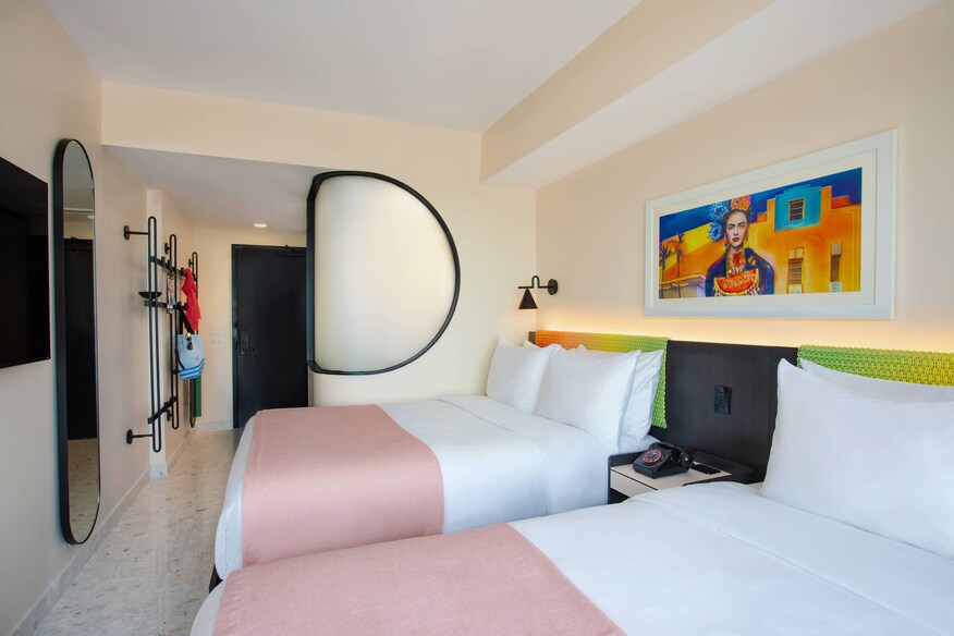 Two queen beds with pink coverlets and multicolored artwork hung above headboards