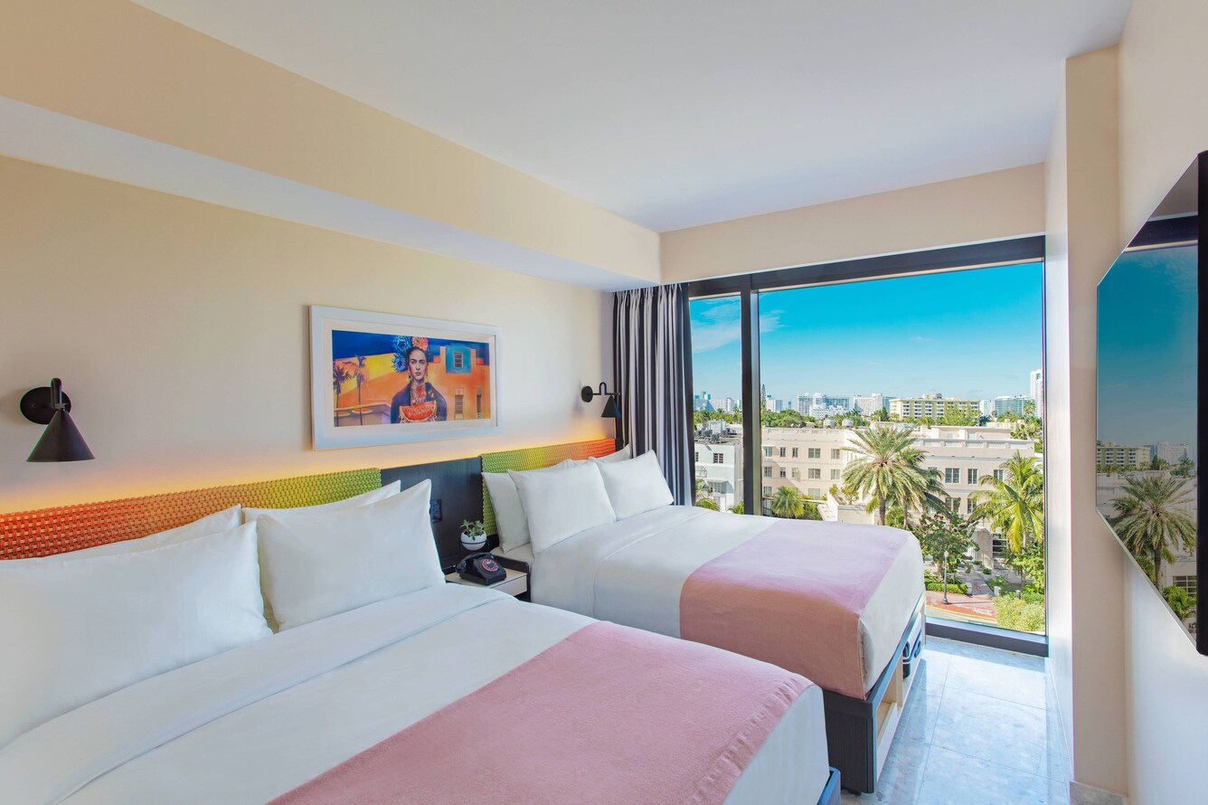 Two queen beds with pink coverlettes, colorful art and view of city