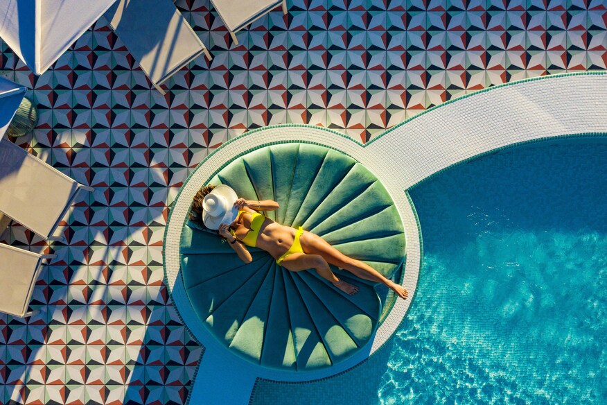 A lady with white hat sunbathing on lily pad day bed.