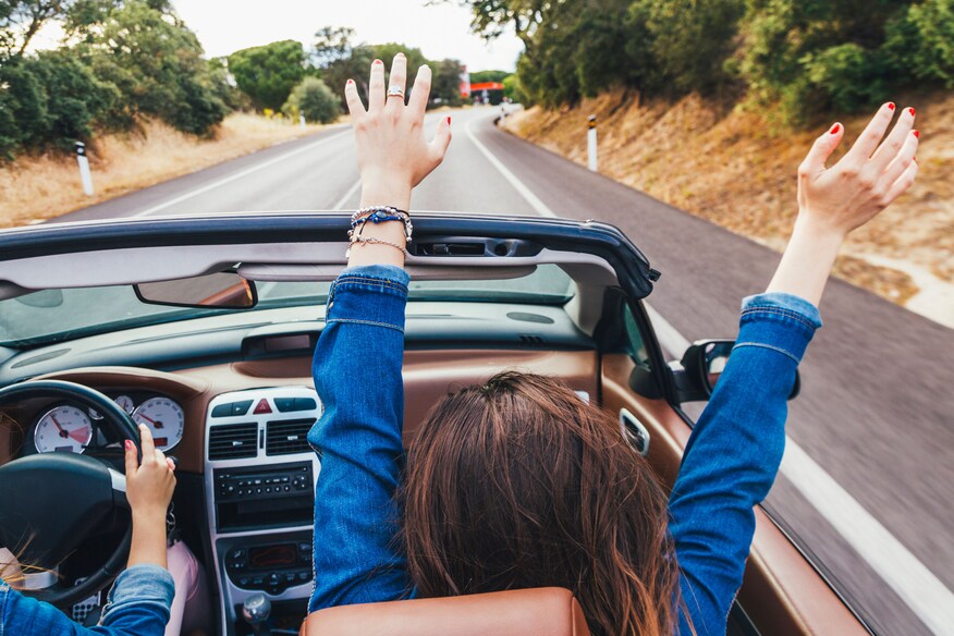 Woman tossing her hands up in the air in front passenger seat wearing a blue jacket.